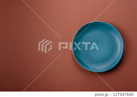 Empty ceramic plate on a monochrome brown background 127687680