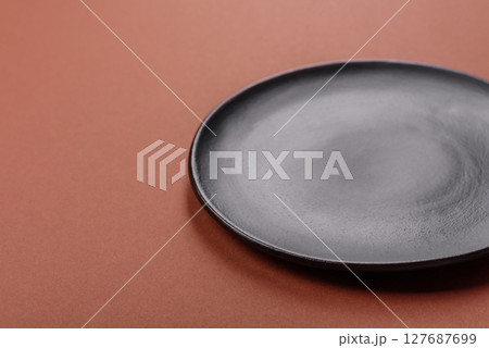 Empty ceramic plate on a monochrome brown background 127687699
