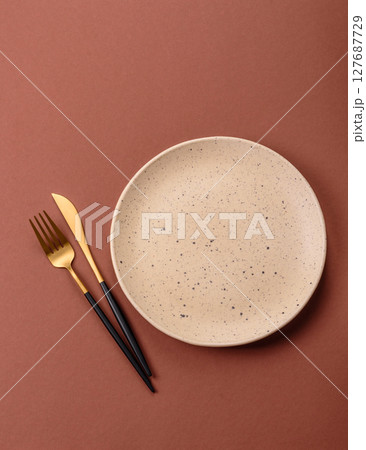 Empty ceramic plate on a monochrome brown background 127687729