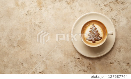 Top view of a cup of coffee with Christmas tree latte art sprinkled with cocoa on beige textured surface. Feeling of festive warmth and coziness 127687744