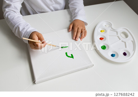 Child painting green brush stroke on canvas with color palette 127688242