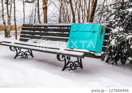 Blue fishing box placed on covered with snow wooden black bench Blue fishing box placed on covered with snow wooden black bench 127688466