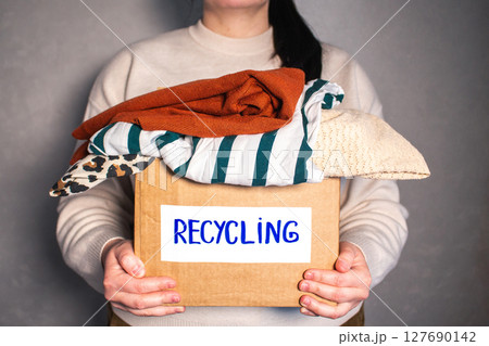 Woman holding cardboard box full of clothes labeled Recycling. Concept of sustainable fashion and responsible wardrobe management. Woman holding cardboard box full of clothes labeled Recycling. Concept of sustainable fashion and responsible wardrobe management. 127690142