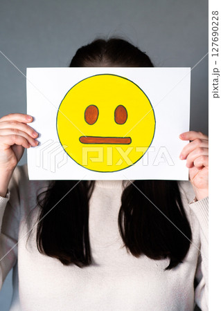 Woman holding emoji mask without smile and any expression in front of face. Social media trends, Gen Z marketing, World emoji day 17 July. Woman holding emoji mask without smile and any expression in front of face. Social media trends, Gen Z marketing, World emoji day 17 July. 127690228