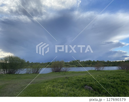 A Serene Lakeside View Featuring Dramatic Sky and Vibrant, Lush Greenery All Around 127690379