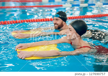 Young cute couple in swimming with boards in the pool 127690757