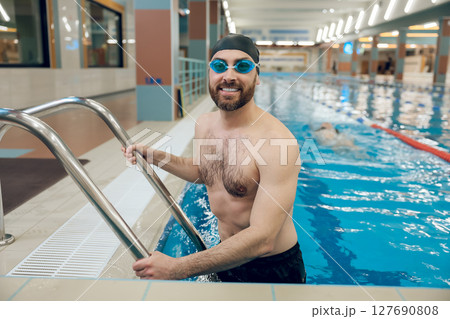 Man in swimming suit and swimming glassed on the ladder in the pool Man in swimming suit and swimming glassed on the ladder in the pool 127690808