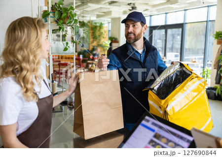 Cafe staff giving takeaway order to delivery courier at counter Cafe staff giving takeaway order to delivery courier at counter 127690844
