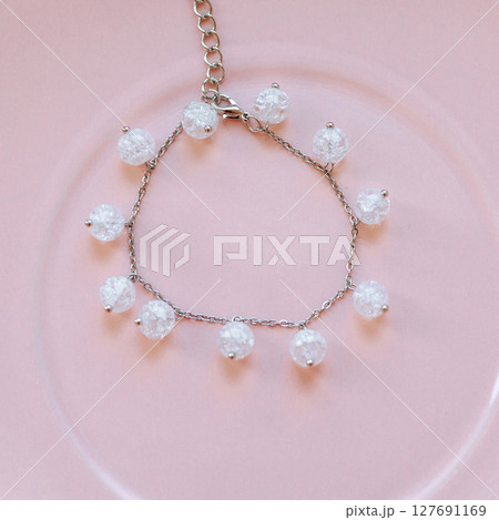 Silver chain bracelet with crackle glass beads on pink ceramic plate, top view, soft lighting Silver chain bracelet with crackle glass beads on pink ceramic plate, top view, soft lighting 127691169