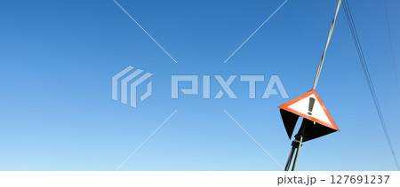 Red triangle with exclamation mark on steel cable of electric pylon, clear sky in background - wide photo, space for text left side 127691237