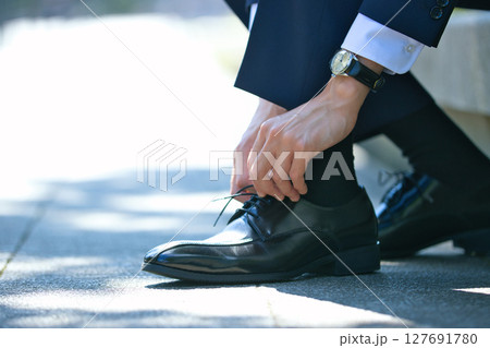 ビジネスシューズの靴紐を結ぶスーツの若い男性の足元 127691780