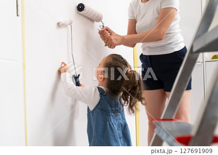 Little girl and her mother painting a wall together with rollers in the living room, family renovation concept.  127691909