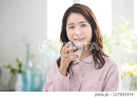 寝起きに水を飲むパジャマの若い女性 127691934