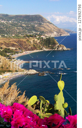 Stunning panoramic view of the blue sea from the top of Capo Vaticano mountain in Calabria, southern Italy. The foreground is adorned with red flowers and vibrant Mediterranean vegetation. Vertical 127692798