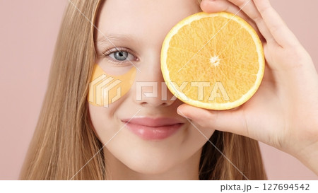 Happy cute young girl with eye patch on studio pink background. Orange. Cute portrait of blonde girl gen Alpha smiling looking at the camera. Concept of cosmetics advertisement for teenagers. Skincare Happy cute young girl with eye patch on studio pink background. Orange. Cute portrait of blonde girl gen Alpha smiling looking at the camera. Concept of cosmetics advertisement for teenagers. Skincare 127694542