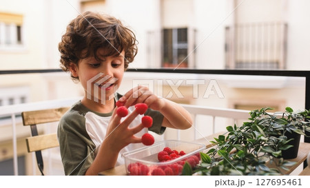 Smiling child playing with raspberries on balcony: healthy eating habits Smiling child playing with raspberries on balcony: healthy eating habits 127695461