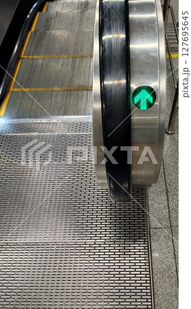 escalator moving up with illuminated green arrow indicating direction at public transport station. 127695645