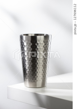 Stainless steel glass on a white table with clean, modern lighting. Stainless steel glass on a white table with clean, modern lighting. 127696112