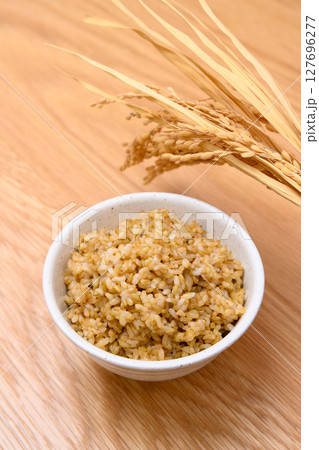 木目テーブル背景の茶碗に玄米ごはんと稲穂 127696277