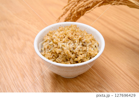 木目テーブル背景の茶碗に玄米ごはんと稲穂 127696429