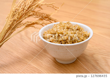 木目テーブル背景の茶碗に玄米ごはんと稲穂 127696435