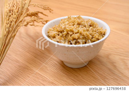 木目テーブル背景の茶碗に玄米ごはんと稲穂 127696438