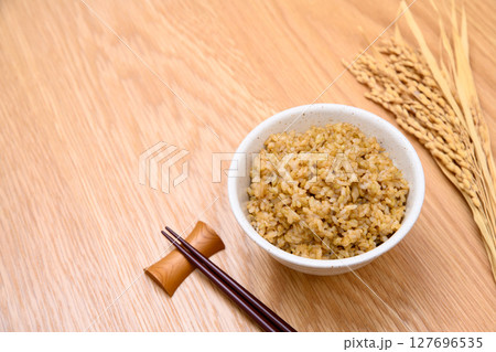 木目テーブル背景の茶碗に玄米ごはんと稲穂 127696535
