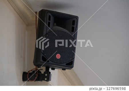 Black public address speaker mounted on white wall near ceiling corner Black public address speaker mounted on white wall near ceiling corner 127696598
