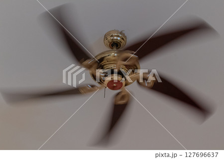 Classic brass ceiling fan with dark wooden blades spinning rapidly overhead 127696637