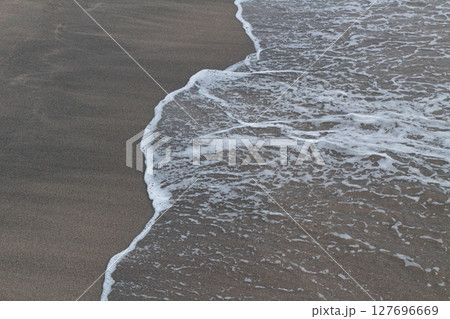 Close-up view of textured white ocean foam meeting dark brown sand 127696669