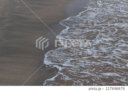 Close-up view of textured white ocean foam meeting dark brown sand Close-up view of textured white ocean foam meeting dark brown sand 127696670