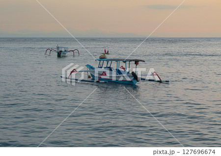 Scenic View of Small Outrigger Boats on Serene Ocean at Sunrise or Sunset Light Scenic View of Small Outrigger Boats on Serene Ocean at Sunrise or Sunset Light 127696674