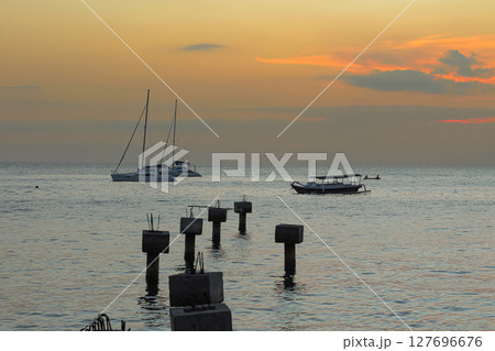 Tranquil ocean scene at dusk showing anchored boats and concrete pillars in water 127696676