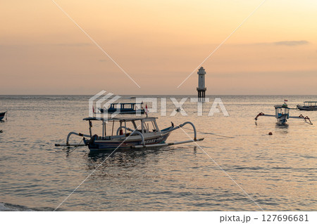 Serene ocean view with fishing boats and distant lighthouse at dusk 127696681