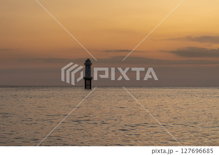 Peaceful coastal landscape with a distant lighthouse against a colorful evening glow 127696685