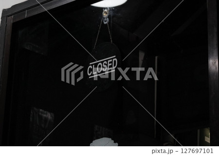 Closed Sign Hanging on Dark Glass Door 127697101