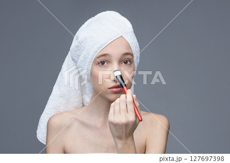 Young caucasian female applying makeup with brush on her face in skincare routin Young caucasian female applying makeup with brush on her face in skincare routin 127697398