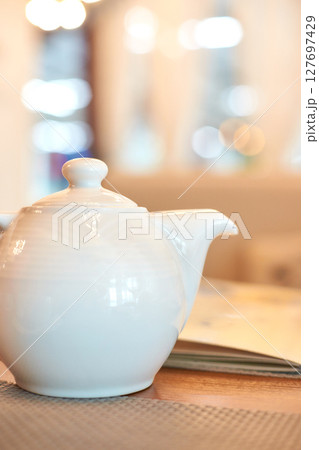 Elegant white teapot on wooden table in brightly lit cafe ambiance Elegant white teapot on wooden table in brightly lit cafe ambiance 127697429