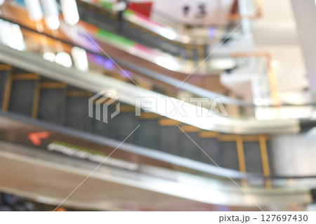 Blurry view of escalators in shopping mall with colorful lights and reflections Blurry view of escalators in shopping mall with colorful lights and reflections 127697430