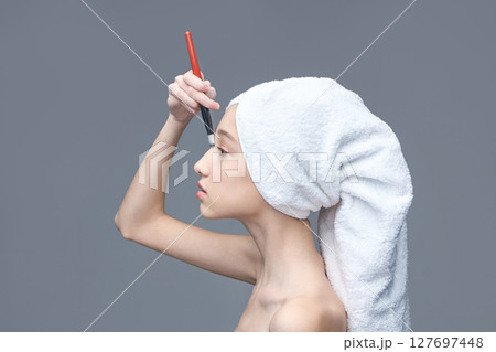 Young caucasian female applying makeup with brush and towel wrapped on her head 127697448