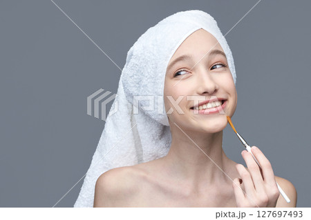 Young caucasian female applying face mask with brush smiling in white towel 127697493