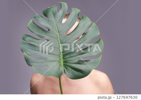 Female with monstera leaf covering face on gray background showcasing natural Female with monstera leaf covering face on gray background showcasing natural 127697630