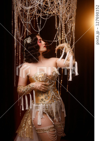 Circus show performer in vintage corset costume under chandelier on dark background Circus show performer in vintage corset costume under chandelier on dark background 127698352