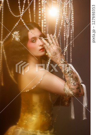 Retro-style performer in vintage costume posing on dark stage under chandelier 127698353