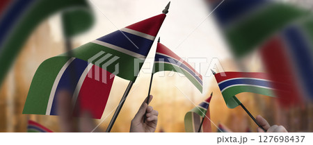 Gambia flags in their hands on a blurred urban background Gambia flags in their hands on a blurred urban background 127698437
