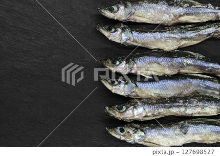 Dry small European smelt fishes on black stone background with copy space Dry small European smelt fishes on black stone background with copy space 127698527