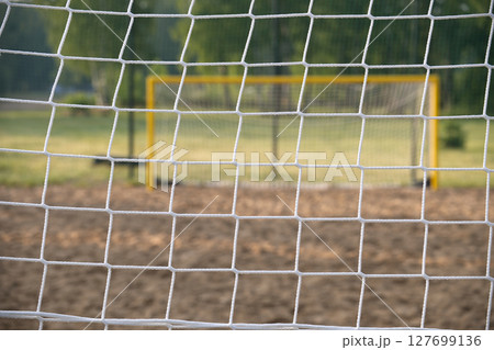 The soccer net is in sharp focus, with a blurred goal post and green field in the background. The soccer net is in sharp focus, with a blurred goal post and green field in the background. 127699136