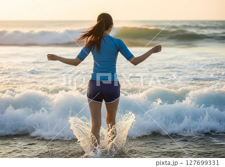 美しく夕焼けに染まる海の波と戯れる女性の後ろ姿 美しく夕焼けに染まる海の波と戯れる女性の後ろ姿 127699331