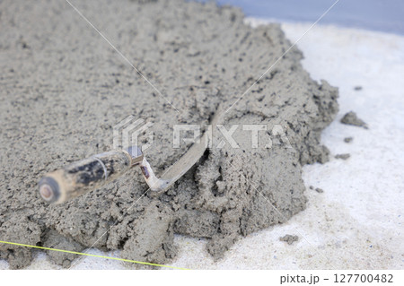 Construction scene featuring a gray concrete surface, a trowel, pull tabs, and wedges used for tile leveling, essential for precision and quality. 127700482