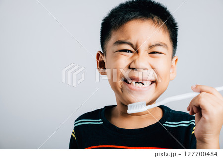 An Asian boy missing an upper milk tooth smiles while holding a toothbrush emphasizing dental care and oral hygiene routine. Isolated on white promoting healthy habits. Children dentist routine 127700484